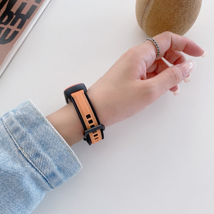 Orange and black silicone wristband worn on wrist, with adjustable clasp and holes