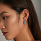 Turquoise square dangle hoop earrings worn on a woman’s ear, silver with blue accents