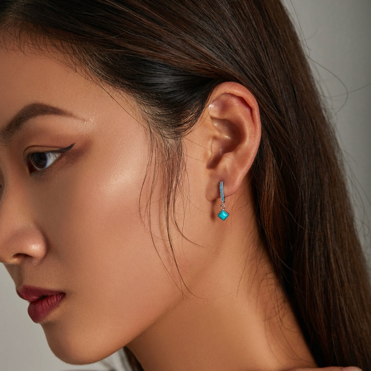 Turquoise square dangle hoop earrings worn on a woman’s ear, silver with blue accents