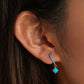 Close-up of turquoise square dangle hoop earrings on ear with silver blue stone band