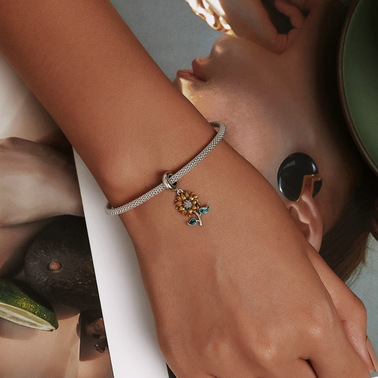 Sunflower charm bracelet on wrist with silver mesh band and green enamel leaf accents