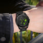 Men's quartz wristwatch with black case, green-accent dial, and black mesh strap.