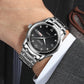 Men's OLEVS quartz watch on wrist, black dial with Roman numerals and date window.
