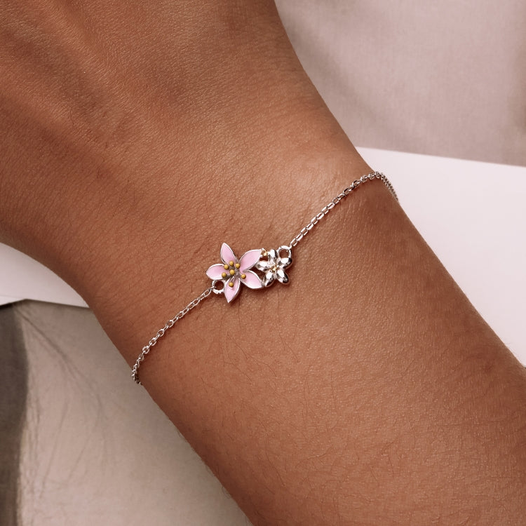 Silver bracelet on wrist with pink cherry blossom flower charm and small leaf accents