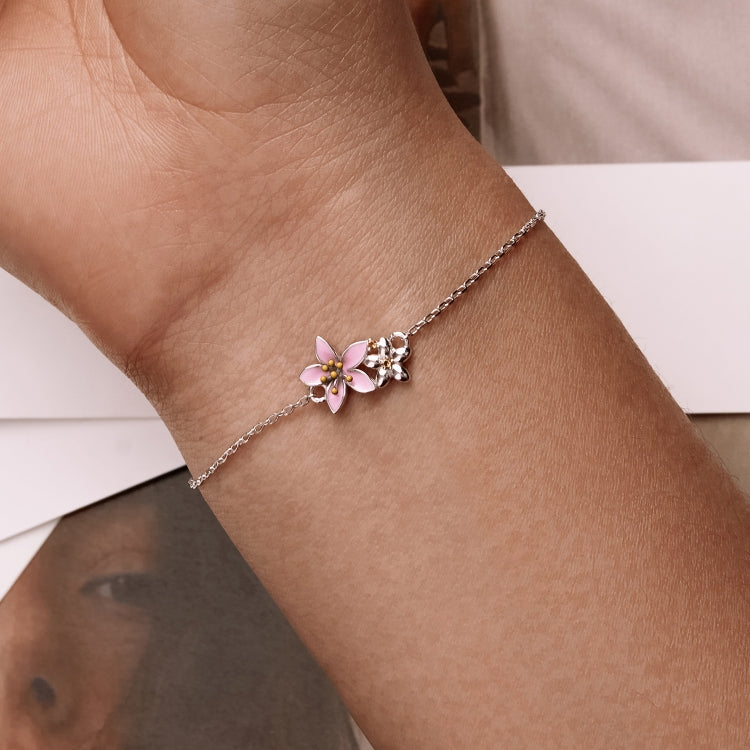 Close-up of silver bracelet on wrist with pink cherry blossom flower charm