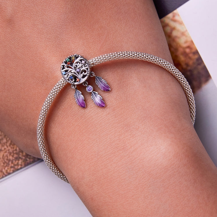 Sterling silver charm bracelet on wrist with round dreamcatcher bead and purple enamel feathers.