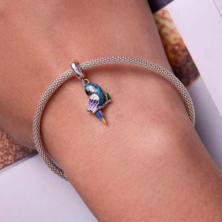 Parrot pendant charm on silver mesh bracelet worn on wrist, turquoise enamel and purple accents