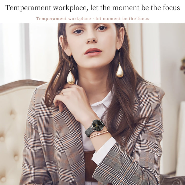 Black dial quartz watch on wrist with mesh steel strap, worn under plaid suit sleeve