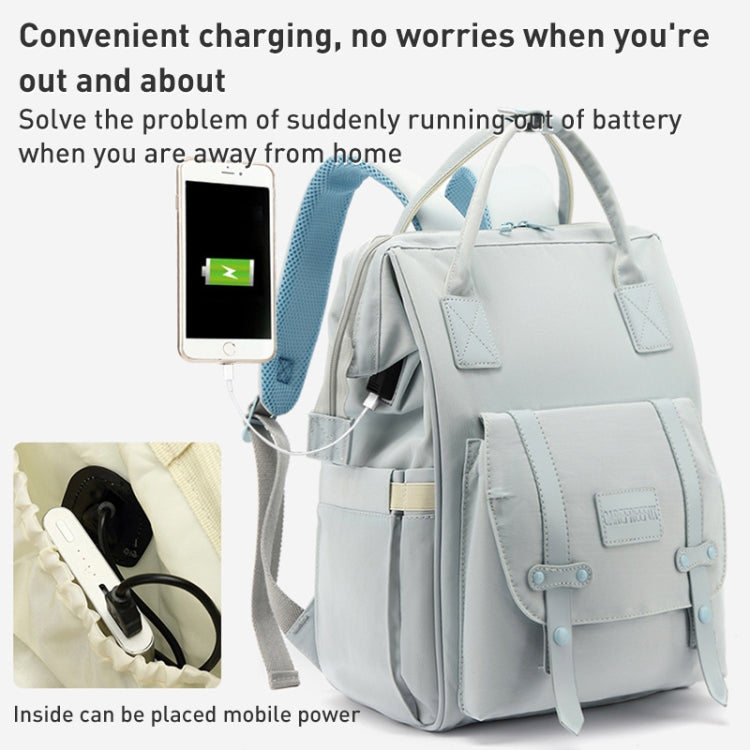 Light blue mommy backpack with front pocket and charging cable beside phone and power bank.