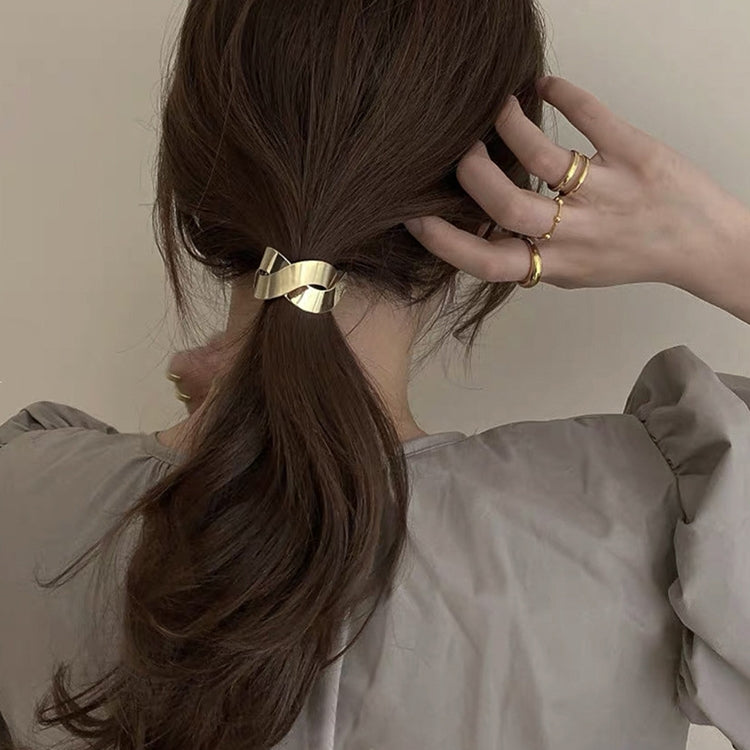 Gold metal bow hair tie on long brown hair, hand adjusting the band