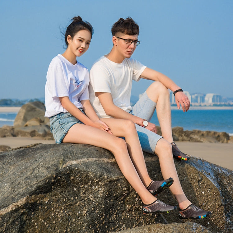 Pair of black swim shoes with colorful geometric prints worn on rocky beach