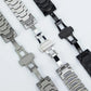 Black and silver watch bands showing their butterfly clasp mechanisms.