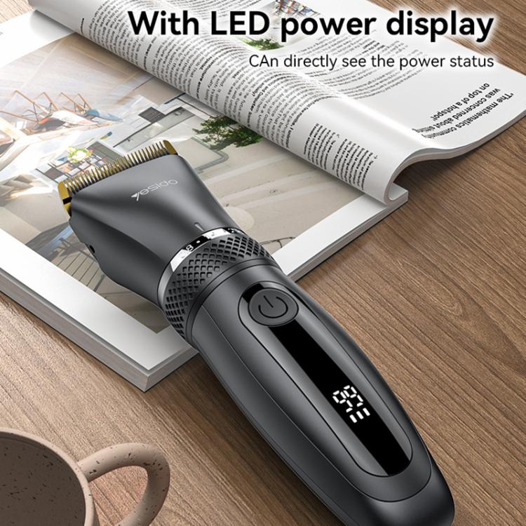 Black cordless hair clipper with LED power display window and gold blade on surface.