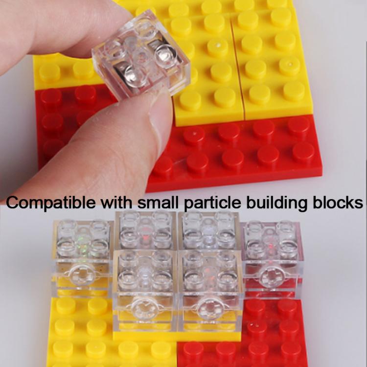 Transparent 2x2 LED building block in hand, mounted on yellow and red stud board