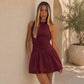 Wine red sleeveless halter mini dress with ruched detailing and flowing tiered hem.