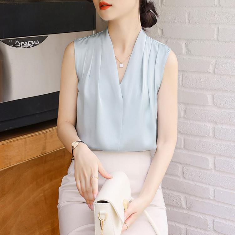 Light blue satin sleeveless V-neck blouse with pleated front; holding a white handbag.