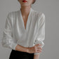 White satin V-neck blouse with long sleeves, vertical drape detail at bodice