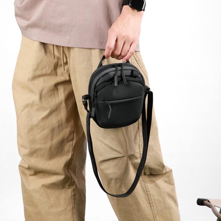 Black small crossbody bag held by hand, adjustable strap and front zip