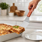 Stainless steel angled spatula with wooden handle, lifting baked lasagna from a dish
