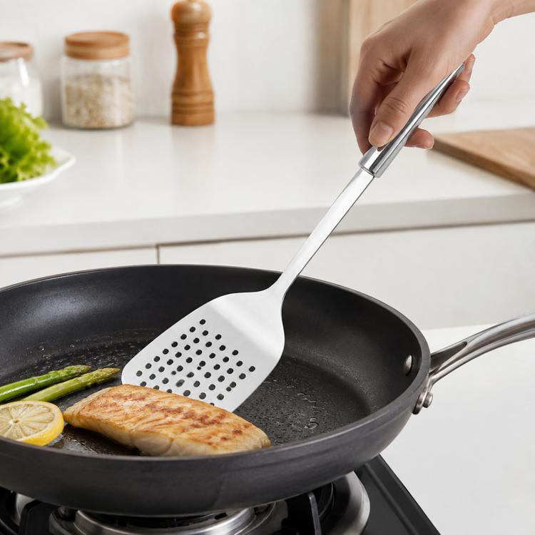 Stainless steel slotted spatula with perforated head for flipping fish in a skillet