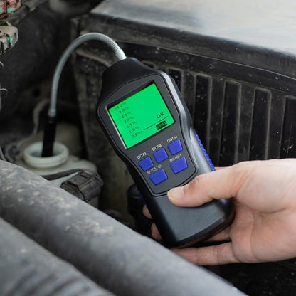 Digital brake fluid tester with green LCD display, hand holding device near engine bay