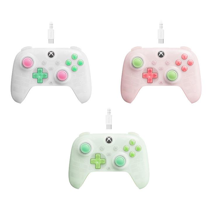 Three translucent wired gaming controllers in white, pink, and green colors