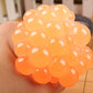 Orange anti-stress grape squeeze ball close-up in hand, glossy translucent texture