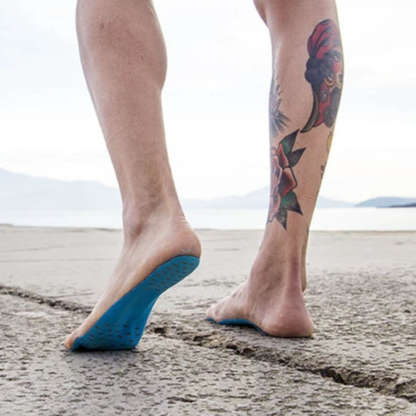Blue anti-slip summer sandal insoles on barefoot feet on a sandy beach