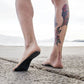 Black dotted anti-slip sandal insoles worn on bare feet on sand