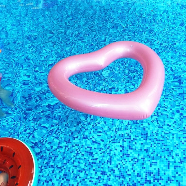 Pink heart-shaped inflatable pool ring on water with visible inner heart opening