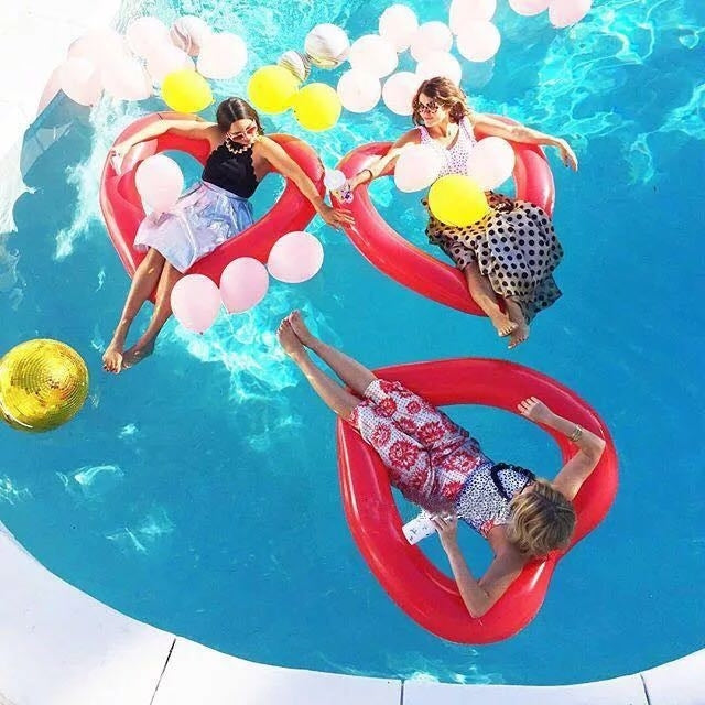 Red heart-shaped inflatable pool ring in water around people