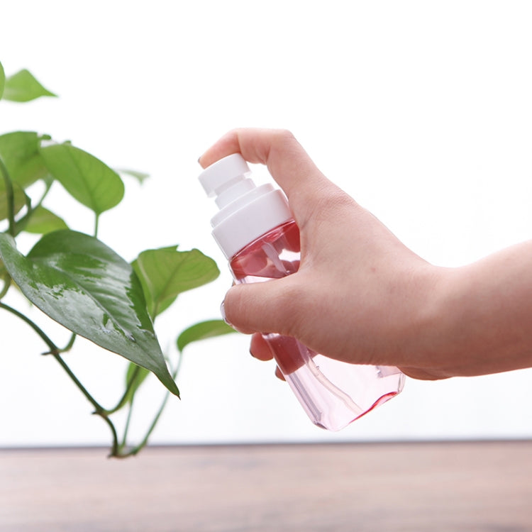 Hand spraying from a refillable transparent bottle with white pump head and pink mist bottle