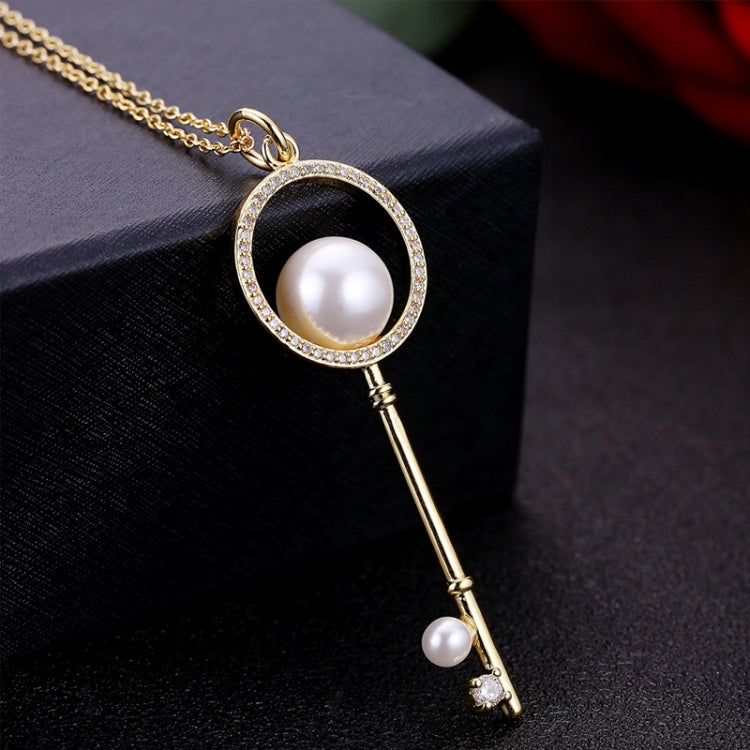 Gold key pendant necklace with circular pearl, rhinestone border, and hanging key charm