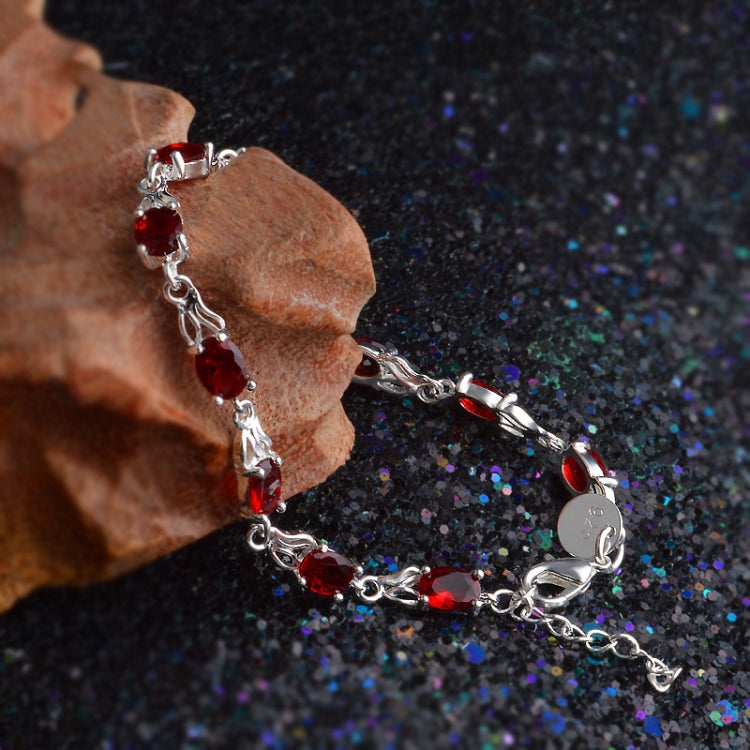Red stone tennis bracelet with silver linked chain and oval gems on hand.