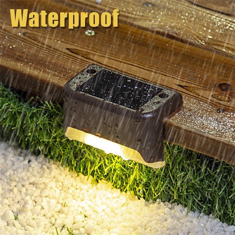 Black solar outdoor step light with warm beam, shown in heavy rain and water droplets.