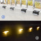 Black solar ground lights casting warm illumination, multiple units spaced along a walkway.