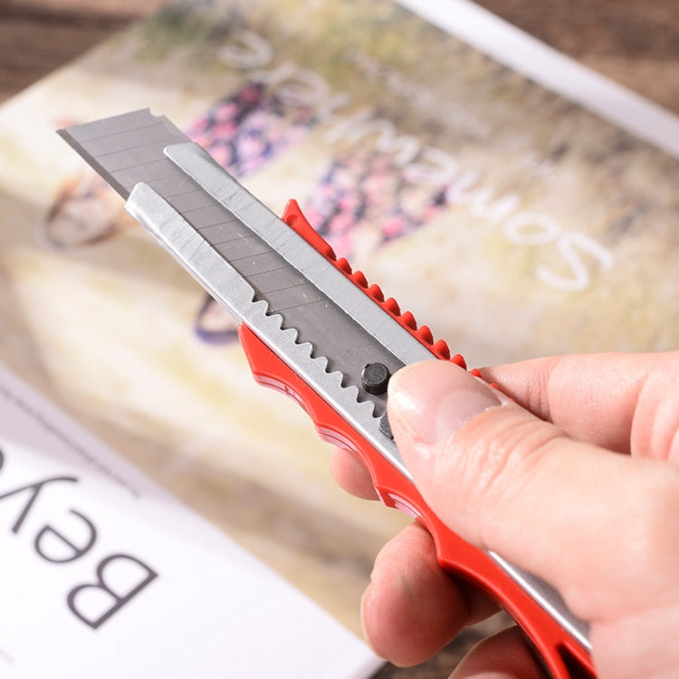 Hand holding red utility paper cutter knife with stainless blade over printed paper