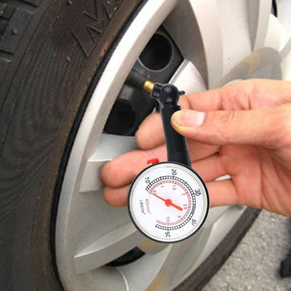 Hand holding a dial tire pressure gauge against a car wheel valve stem