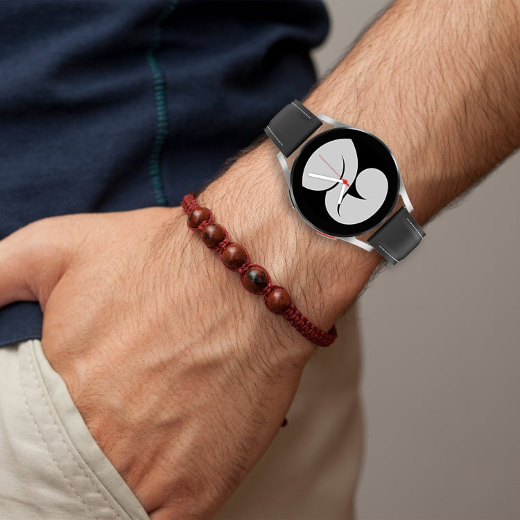 Black watch band on wrist with metal buckle and perforated stitching.