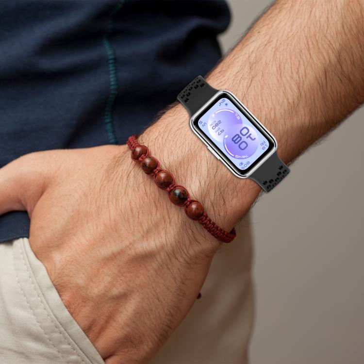 Black perforated silicone watch band worn on a wrist beside a beaded bracelet.