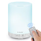 Ultrasonic essential oil diffuser with blue LED glow and light gray wood-grain base, remote shown