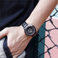 Men's steel bracelet watch on wrist with black dial, red ring detail, and bezel.