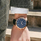 Multi-function quartz wristwatch with blue dial, dark strap, and rose gold-tone case