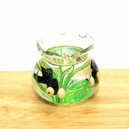 Miniature transparent glass fish tank with green plants and small black fish