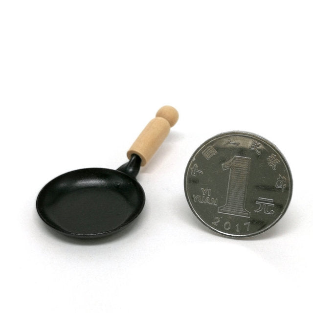 Miniature black frying pan with wooden handle, shown with coin size reference