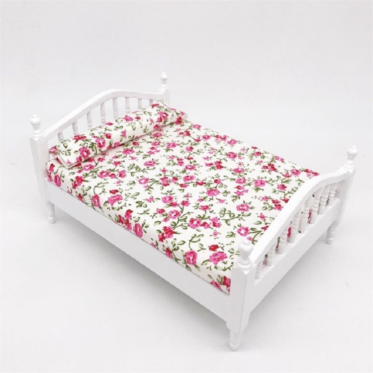 Angle view of white mini doll bed with floral fitted bedding and slatted headboard
