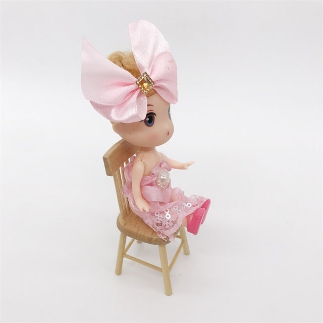 Doll seated on miniature wooden dollhouse chair with slatted back.