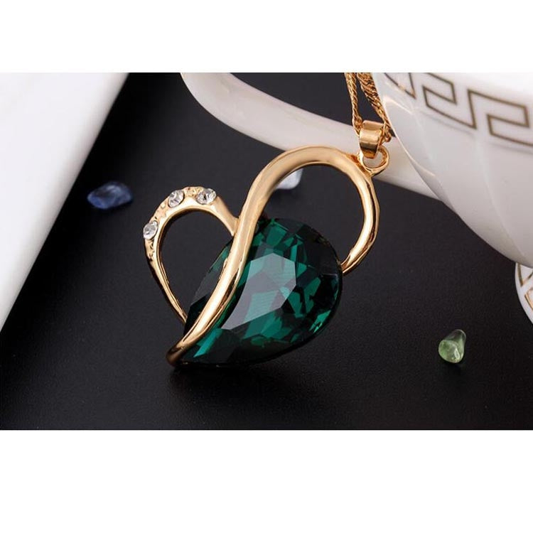 Gold-tone heart crystal pendant with green faceted stone, close-up