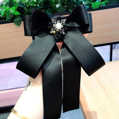 Black satin bow brooch with rhinestone and pearl centerpiece, attached pin back.