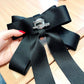 Black satin bow brooch detail with silver clasp pin and rhinestone pearl center.